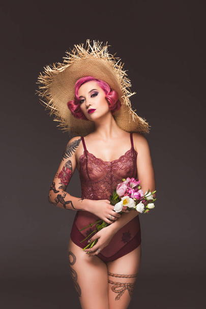pretty tattoed girl in lingerie and straw hat with flowers infront of grey background  - Fotó, kép