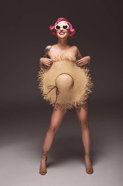 beautiful naked pink haired woman in sunglasses covering by straw hat infront of grey background - Fotografie, Obrázek