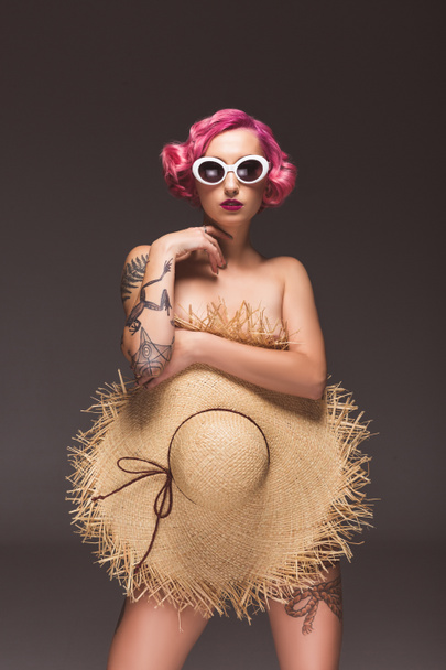 beautiful naked pin up girl in sunglasses covering by straw hat infront of grey background - Фото, изображение