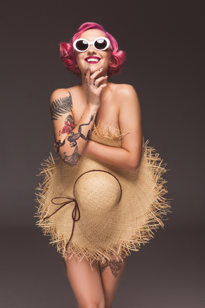 beautiful naked pin up girl in sunglasses covering by straw hat infront of grey background - Photo, Image