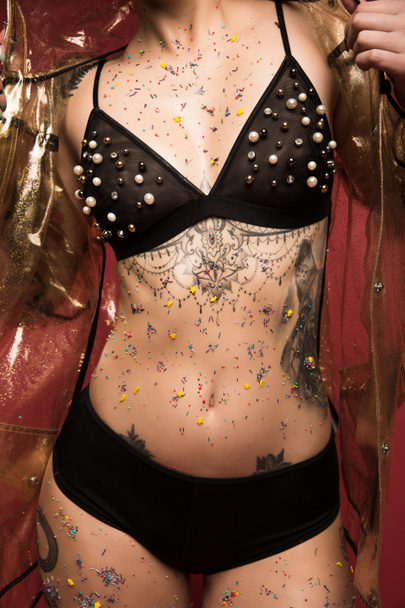 cropped image of female body with tattoos in lingerie and raincoat infront of red background - Foto, imagen