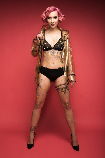 beautiful pink haired girl with tattoos in lingerie and raincoat infront of red background - Zdjęcie, obraz