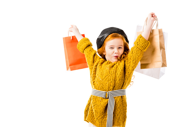 παιδί ευτυχισμένη κόκκινα μαλλιά, κρατώντας τσάντες για ψώνια στα χέρια πάνω από το κεφάλι που απομονώνονται σε λευκό - Φωτογραφία, εικόνα