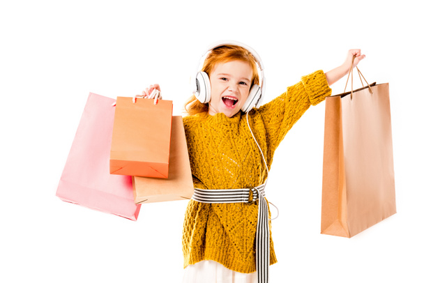 Rotschopfiges Kind singt und hält Einkaufstüten isoliert auf weißem Grund - Foto, Bild