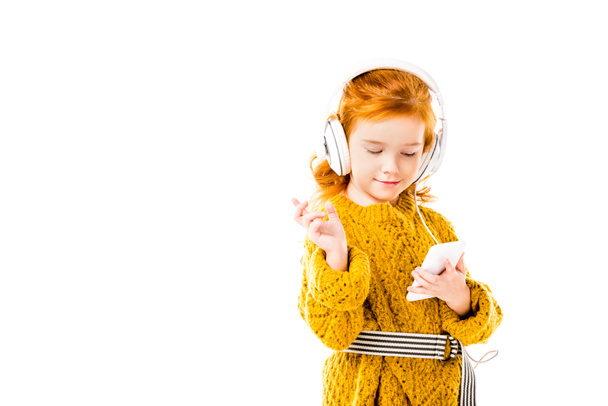 niño de pelo rojo escuchando música con teléfono inteligente aislado en blanco
 - Foto, Imagen