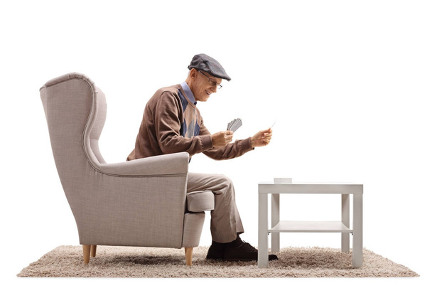 Senior playing cards by himself in an armchair  - Photo, Image