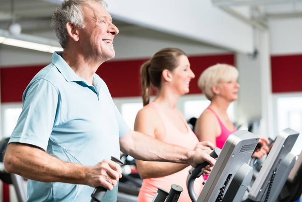 Seniors train on cross trainer with personal trainer at the gym - Photo, Image