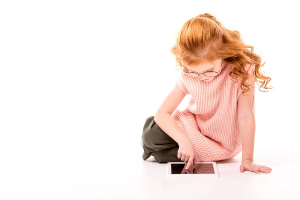 παιδί με τζίντζερ μαλλιών κάθεται και χρησιμοποιώντας tablet σε λευκό - Φωτογραφία, εικόνα
