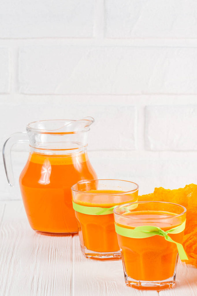 Pumpkin fresh juice in beautiful glasses and jug with pieces of ripe vegetable on white wooden background. Sweet orange juice. Healthy eating, diet theme. Close up photography. Vertical banner - Photo, Image