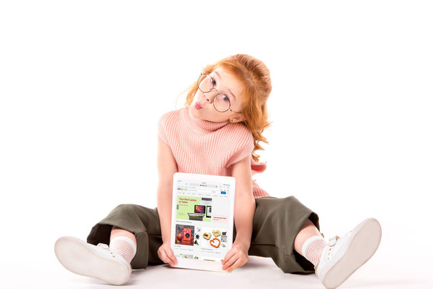 red hair child sitting and holding tablet with loaded ebay page on white - 写真・画像