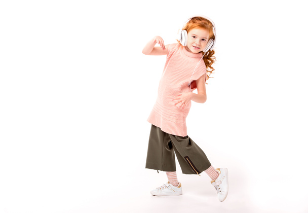 red hair kid in headphones dancing and looking at camera on white - Foto, Imagen