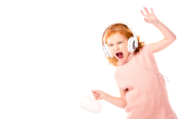 red hair kid in headphones screaming and dancing with cup isolated on white - Photo, Image
