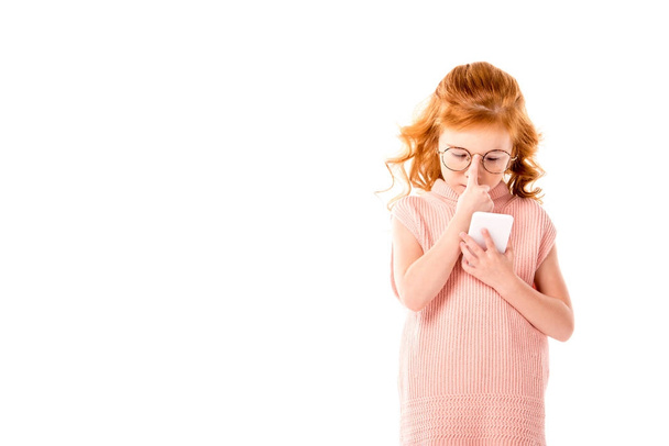 niño de pelo rojo reflexivo mirando teléfono inteligente aislado en blanco
 - Foto, imagen