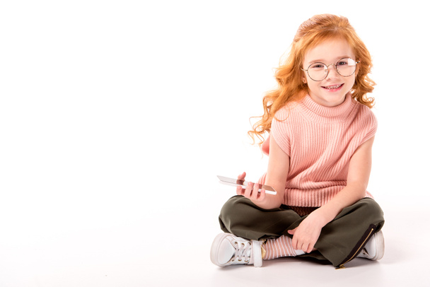 niño con el pelo de jengibre sentado y sosteniendo el teléfono inteligente en blanco
 - Foto, imagen