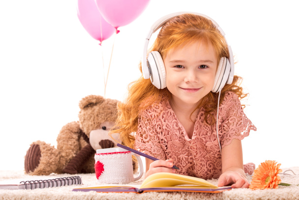 Lächeln rotes Haar Kind mit Kopfhörern Blick auf Kamera isoliert auf weiß - Foto, Bild