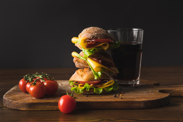 big sandwich with cheese, cherry tomatoes and glass of cola on cutting board - Фото, зображення