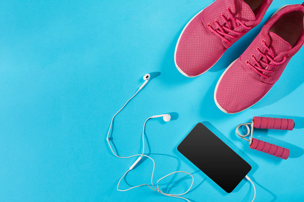 Flat lay shot of Sport equipment. Sneakers, earphones and phone on blue background. - Photo, Image