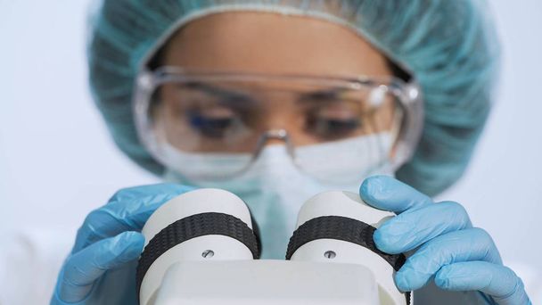 Mixed race woman looking into microscope, doing biochemical research, closeup - Photo, image