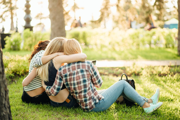 Back view of three beautiful women sitting on grass and hugs - Photo, Image