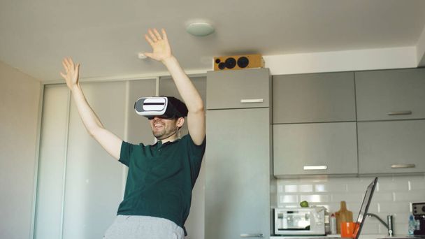Funny young man in virtual reality 360 headset dancing in kitchen in the morning while listening to music and have fun at home - 写真・画像