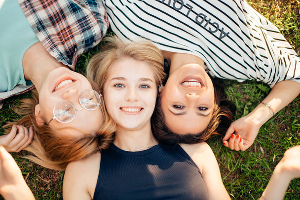 Top view of stylish friends looking at camera and smiling while lying on grass - Fotoğraf, Görsel