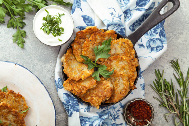 Potato latkes traditional jewish pancakes with sour cream, parsley, dry red pepper flakes and mint sauce. Background, white napkin with blue flowers. Hannukah celebration dish concept. - Foto, imagen