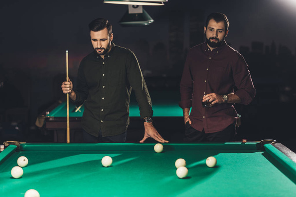 couple of successful men standing beside pool table with drink at bar - Φωτογραφία, εικόνα