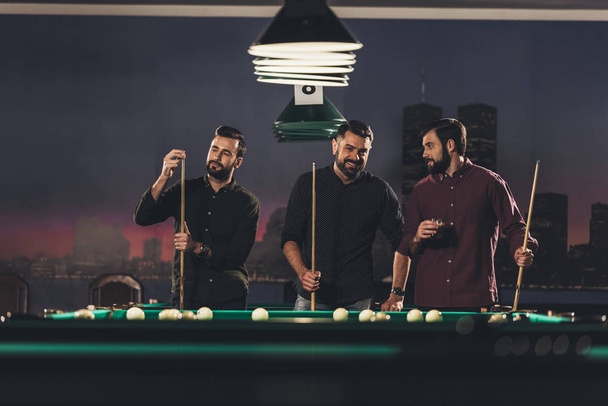 company of successful handsome men standing beside pool table with drink at bar   - Photo, Image