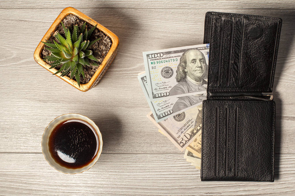 Black leather wallet with dollar bills, cup of coffee and housep - Photo, Image