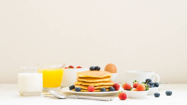 Desayuno saludable con panqueque y granola con arándanos y fresas y café negro, leche y jugo de naranja sobre fondo de mesa de piedra blanca
 - Foto, imagen