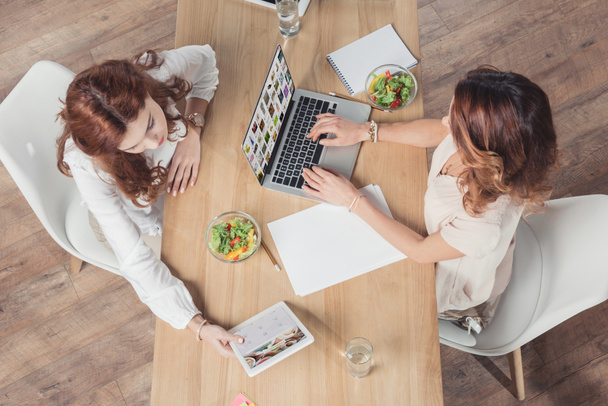 Ansicht von Geschäftsfrauen, die gemeinsam zu Mittag essen und Laptop und Tablet im Büro benutzen - Foto, Bild