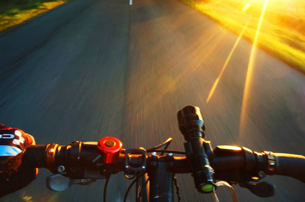 Βόλτα με ποδήλατο το βράδυ καλοκαίρι στο ηλιοβασίλεμα, ένα τροχό ενός ποδηλάτου στην κίνηση κινηματογράφηση σε πρώτο πλάνο - Φωτογραφία, εικόνα