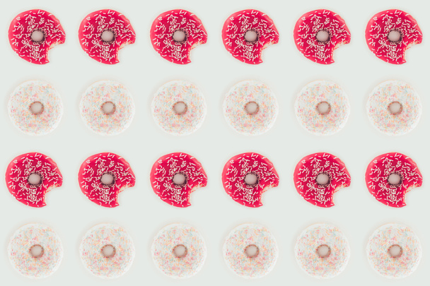 bovenaanzicht van naadloze patroon van rijen van roze en witte lekkere donuts geïsoleerd op wit - Foto, afbeelding