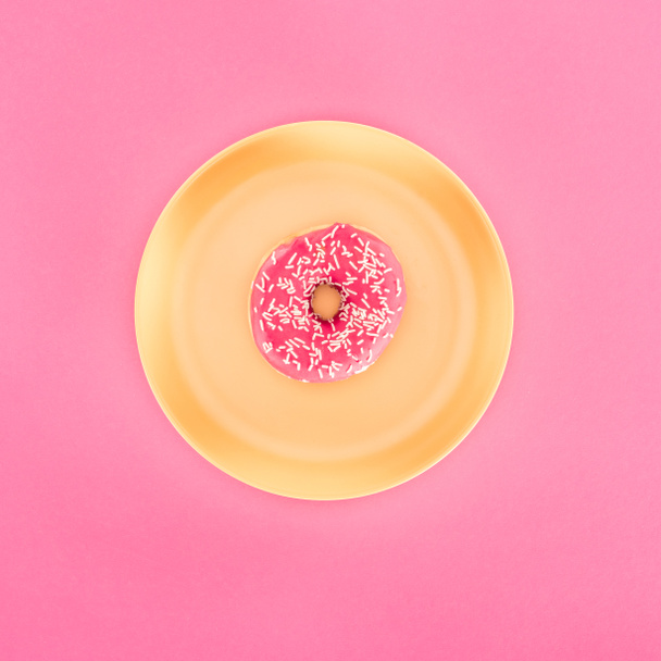 top view of pink glazed doughnut on yellow plate isolated on pink - Foto, Imagen