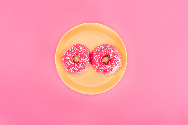 top view of pink glazed doughnuts on yellow plate isolated on pink - Valokuva, kuva