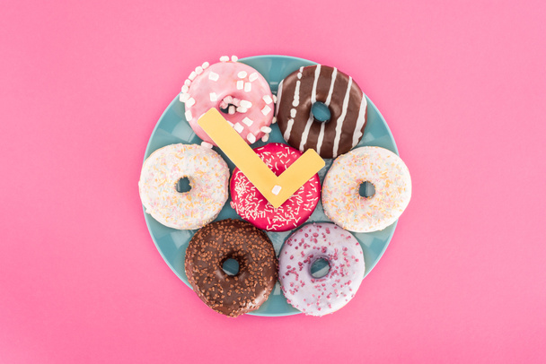Vista superior do relógio feito de donuts na placa isolada em rosa
 - Foto, Imagem