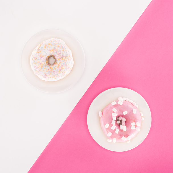 bovenaanzicht van verschillende geglazuurde donuts op vergulde op witte en roze ondergrond. - Foto, afbeelding