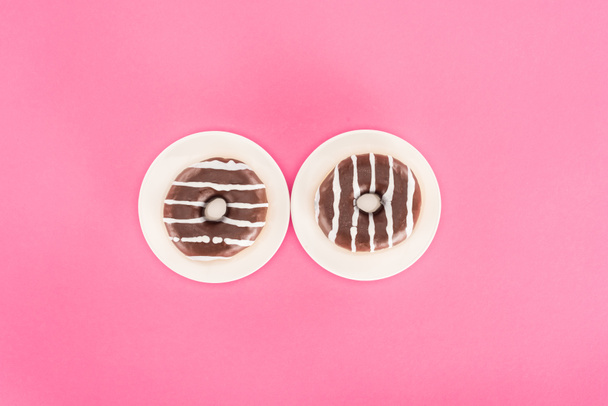 bovenaanzicht van donuts geglazuurd met chocolade op platen geïsoleerd op roze - Foto, afbeelding