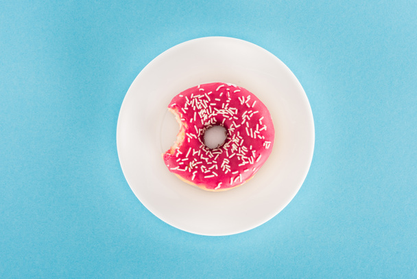 bovenaanzicht van gebeten roze geglazuurde donut op plaat - Foto, afbeelding