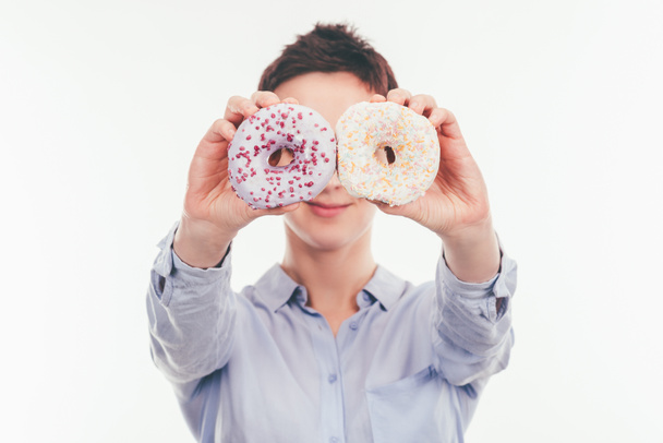 smiling woman covering eyes with tasty doughnuts isolated on white - Photo, Image