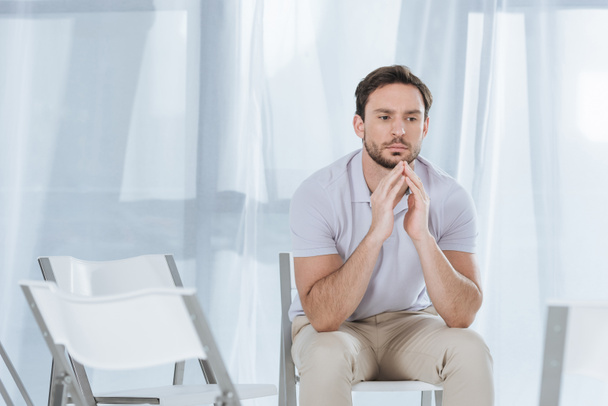 depressed middle aged man sitting on chair and looking away in empty room - Photo, Image