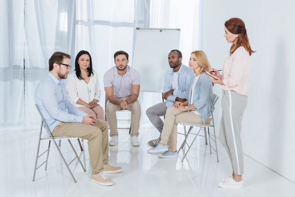 not defterinde yazılı ve grup terapisi sırasında sandalyelere oturan çok ırklı insanlarla konuşurken psikoterapist  - Fotoğraf, Görsel