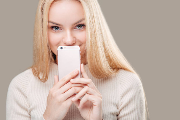 жінка покриває рот порожнім екраном смартфона на сірому фоні
 - Фото, зображення