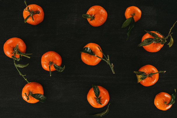 flat lay of arrangement of mandarins with leaves on black wooden surface - Foto, immagini