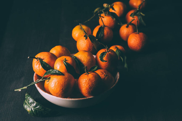 close up view of mandarins in bowl on dark wooden tabletop - Photo, Image