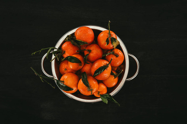 top view of pile of mandarins in saucepan on black wooden surface - 写真・画像