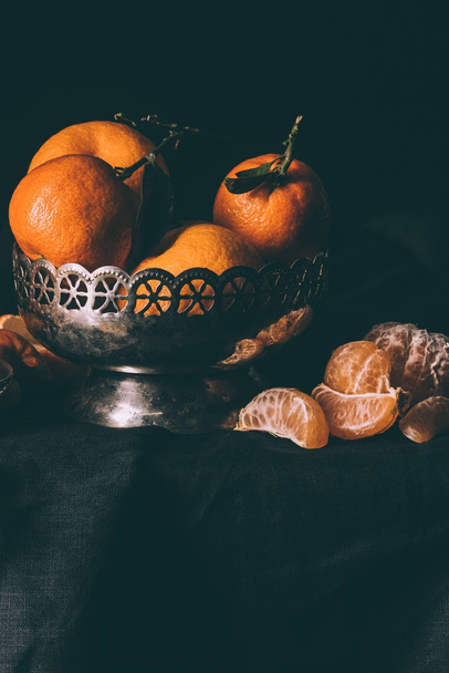 close up view of fresh mandarins in metal bowl on table with dark tablecloth - Фото, изображение