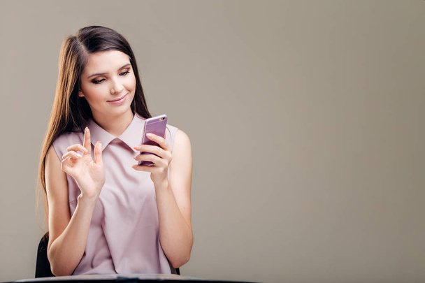 Portrait of a smiling casual woman holding smartphone over white background - Φωτογραφία, εικόνα