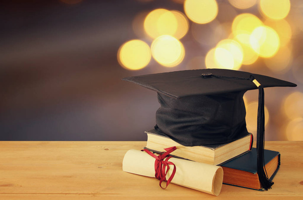 Image of graduation black hat over old books next to graduation on wooden desk. Education and back to school concept - Photo, Image