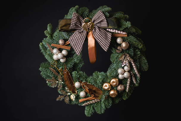 close-up of Christmas wreath with green fir tree branches, brown bow and beautiful decoration on black background - Fotó, kép